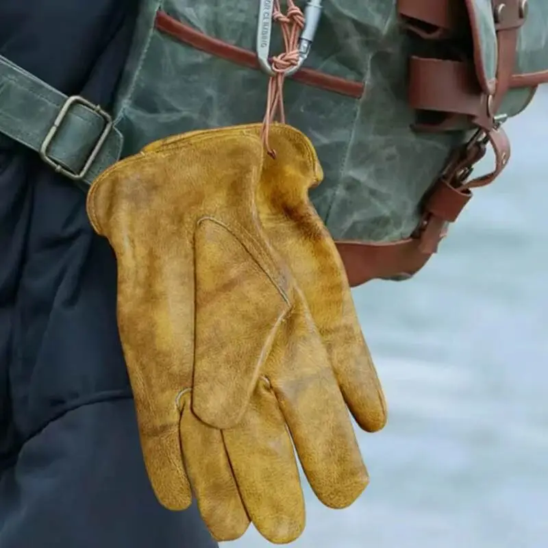 Golden suede leather safety gloves hanging from a hiking bag.
