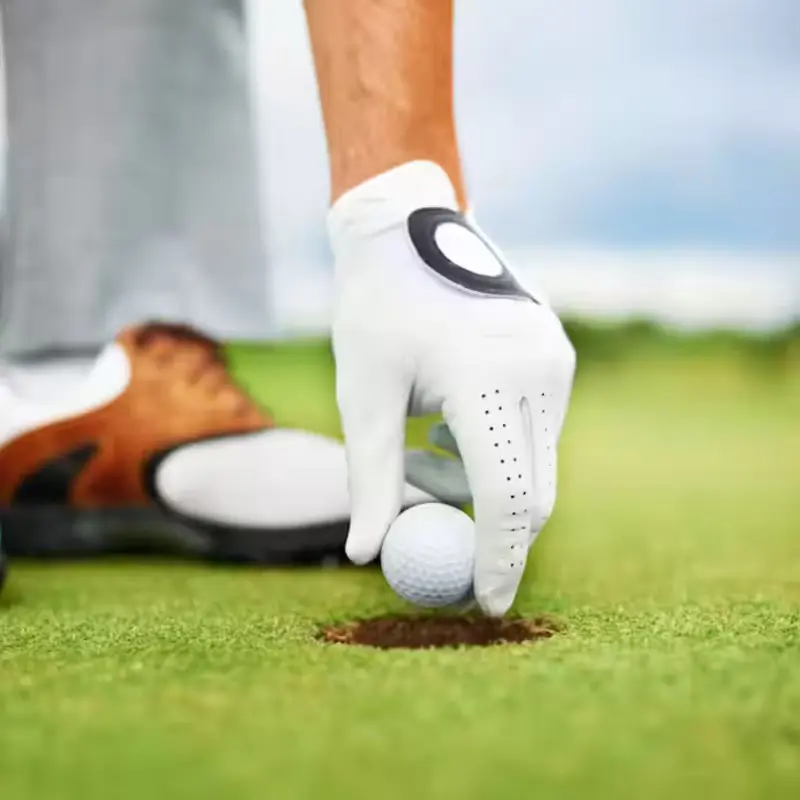 Golfer wearing a white glove placing a ball in the hole.