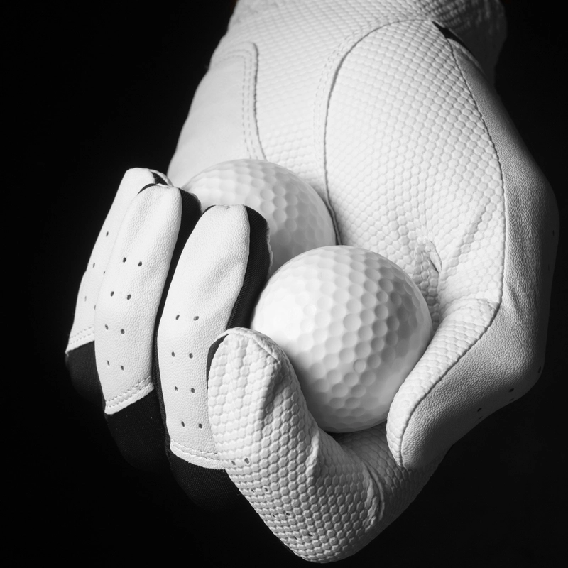 White golf glove holding two golf balls against a black background